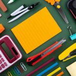 Stationery including a calculator, scissors, stapler, and notepad on a green surface