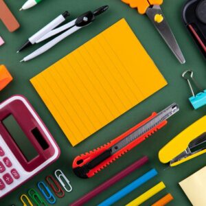 Stationery including a calculator, scissors, stapler, and notepad on a green surface
